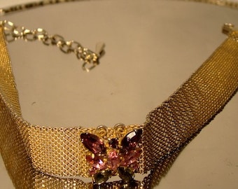 May include: A gold mesh choker necklace with a pink and purple butterfly-shaped rhinestone embellishment.