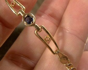 May include: A gold bracelet with a single blue gemstone set in a square frame. The bracelet has a chain link design.
