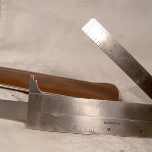 May include: A silver folding ruler with a brown leather case. The ruler has a protractor and inch markings. The ruler is open to 90 degrees.