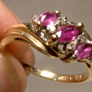 May include: A gold ring with three pink gemstones and smaller clear gemstones set in a twisted band.