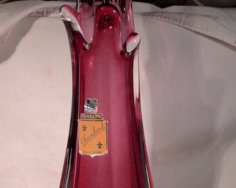Puede incluir: Un jarrón de vidrio alto de color burdeos con una base de vidrio transparente. El jarrón tiene una forma orgánica única y está etiquetado como "Murano Chambord Flli Toso".