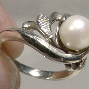 May include: A silver ring with a white pearl set in a leaf design.