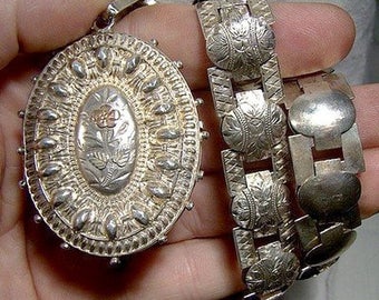 May include: A silver locket with an ornate design and a floral pattern inside. The locket is attached to a silver chain with a similar design.