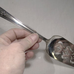 May include: Silver cake server with a decorative cut-out design. The handle is ornate and has a beaded edge.