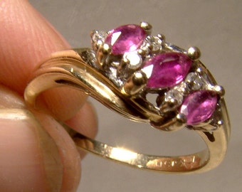 May include: A gold ring with three pink gemstones and smaller clear gemstones set in a twisted band.