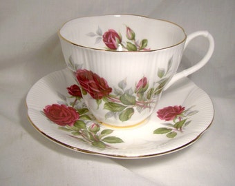 May include: A white teacup and saucer set with a gold trim and a floral design featuring red roses and green leaves.