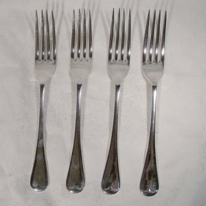 May include: Four silver forks with ornate handles. The forks are arranged in a row on a white surface.