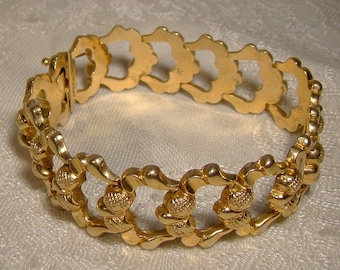 May include: A gold-toned bracelet with a delicate, intricate design. The bracelet is made of linked, open-work, flower-shaped pieces.