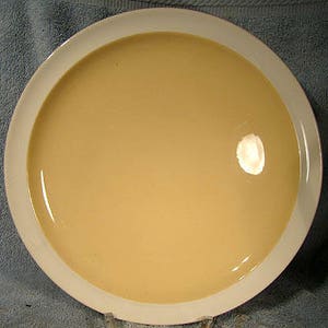May include: A white ceramic dinner plate with a wide rim and a pale yellow centre.