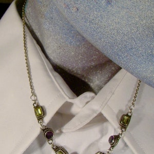 May include: A silver chain necklace with alternating purple and green gemstone accents.