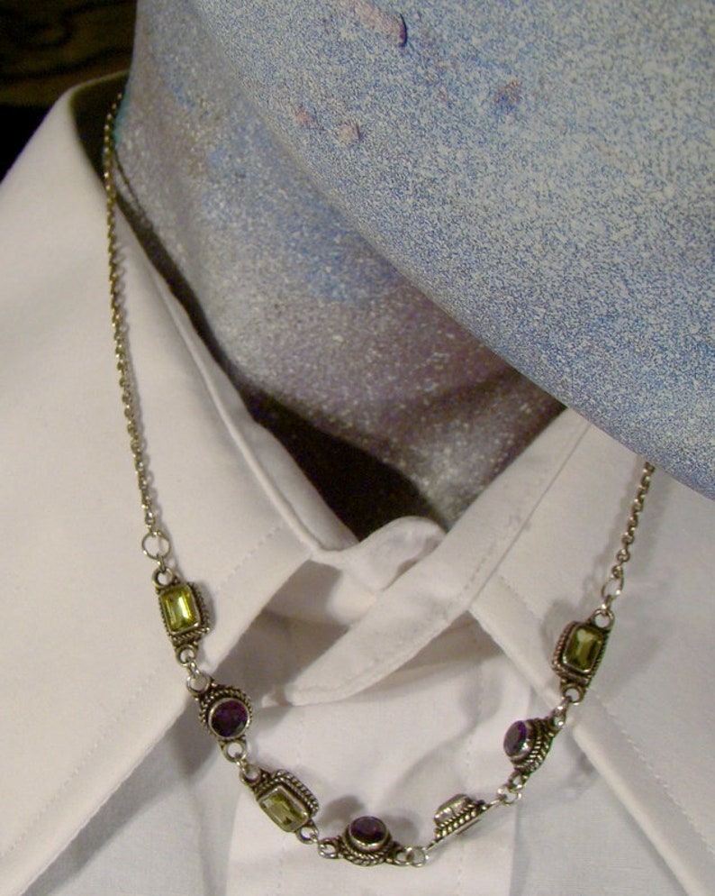 May include: A silver chain necklace with alternating purple and green gemstone accents.