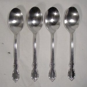 May include: Four silver spoons with ornate handles. The spoons are polished and shiny.