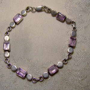 Puede incluir: Un brazalete de plata con un dise&ntilde;o de cadena y piedras preciosas rectangulares de color p&uacute;rpura.