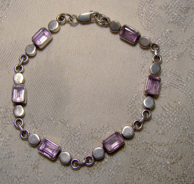 Puede incluir: Un brazalete de plata con un dise&ntilde;o de cadena y piedras preciosas rectangulares de color p&uacute;rpura.