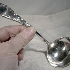 May include: A silver ladle with an ornate handle. The ladle has a rounded bowl and a long, slender handle with a decorative design.