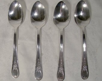 May include: Four silver spoons with ornate designs on the handles. The spoons are arranged in a row on a white surface.