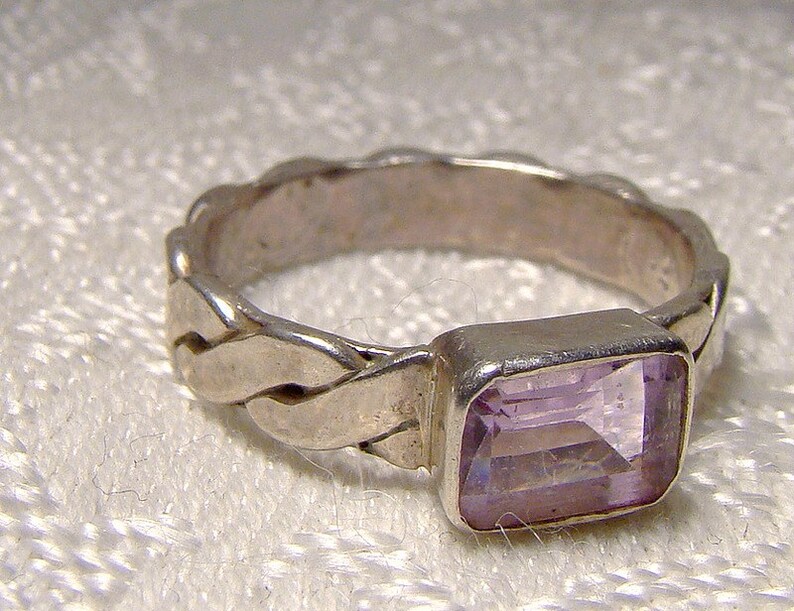 May include: A silver ring with a braided band and a light purple rectangular gemstone.
