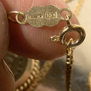 May include: Close-up of a gold chain with a 10K hallmark. The chain is made of small, linked circles.