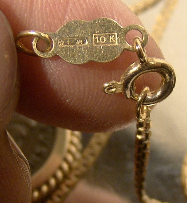 May include: Close-up of a gold chain with a 10K hallmark. The chain is made of small, linked circles.