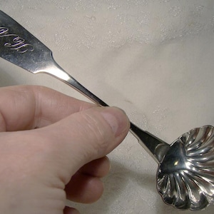 May include: A silver spoon with a shell-shaped bowl and a long handle. The handle is engraved with the letters "J.B."