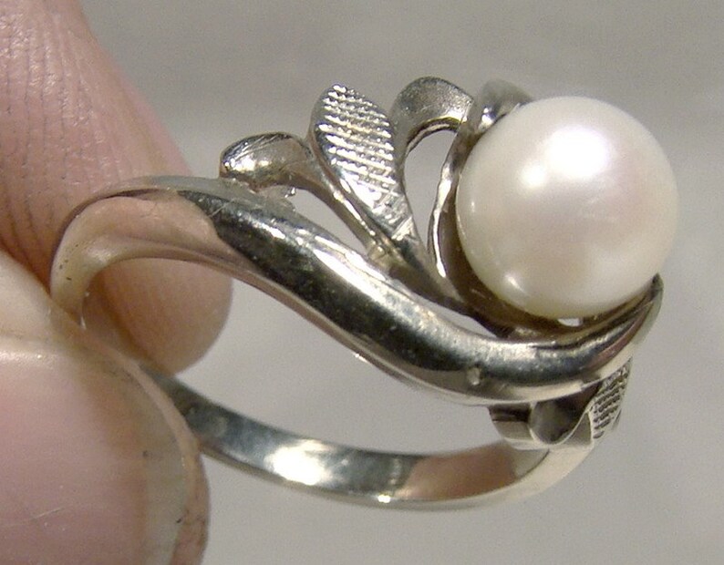 May include: A silver ring with a white pearl set in a leaf design.