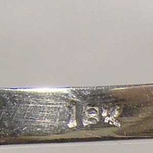 May include: Close-up of the inside of a silver ring with the inscription "18K" on the band.