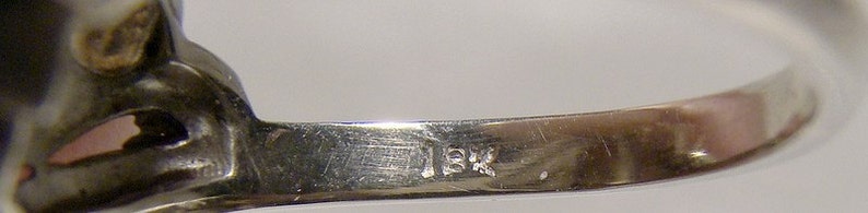 May include: Close-up of the inside of a silver ring with the inscription "18K" on the band.