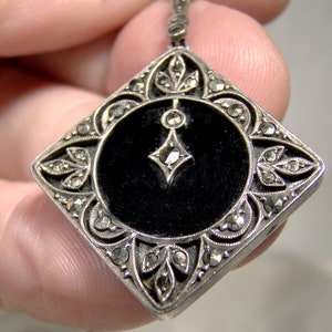 May include: A silver pendant with a black enamel center and a geometric design. The pendant is decorated with marcasite stones.
