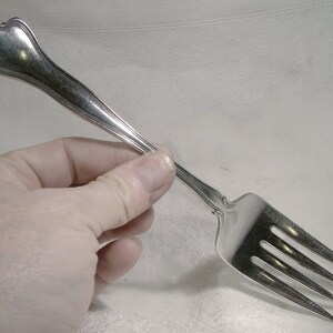 May include: A silver fork with a decorative handle and three tines. The fork is held in a hand.