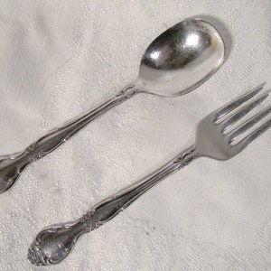 May include: A set of silver-plated baby cutlery, including a spoon and fork, with ornate handles.