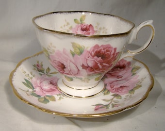 May include: A white teacup and saucer set with a pink rose floral pattern and gold trim.