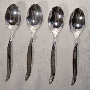May include: Four silver spoons with ornate handles. The spoons are polished and reflect light.