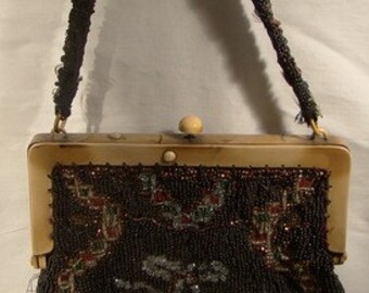 May include: A vintage beaded purse with a black and green beaded design featuring a mushroom motif. The purse has a brown frame and a cream-colored clasp.