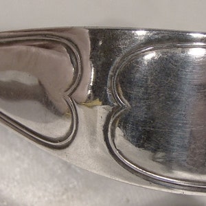 Puede incluir: Pinzas de servir de plata con un dise&ntilde;o en forma de coraz&oacute;n. Las pinzas est&aacute;n hechas de plata pulida y tienen una superficie lisa y redondeada.