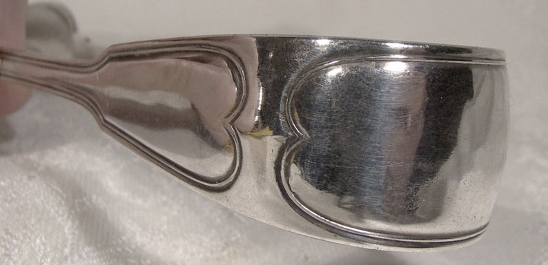 Puede incluir: Pinzas de servir de plata con un dise&ntilde;o en forma de coraz&oacute;n. Las pinzas est&aacute;n hechas de plata pulida y tienen una superficie lisa y redondeada.