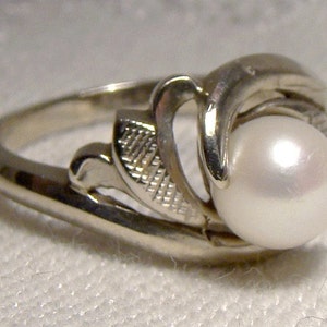 May include: A silver ring with a pearl set in a delicate floral design.