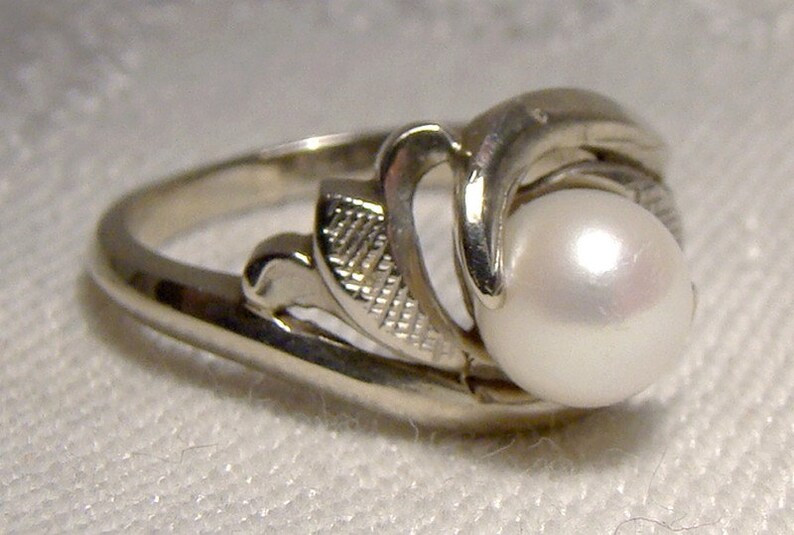May include: A silver ring with a pearl set in a delicate floral design.