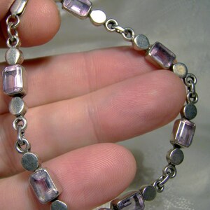 Puede incluir: Un brazalete de cadena de plata con piedras de amatista rectangulares. El brazalete tiene un dise&ntilde;o simple con c&iacute;rculos de plata y piedras de amatista alternos.
