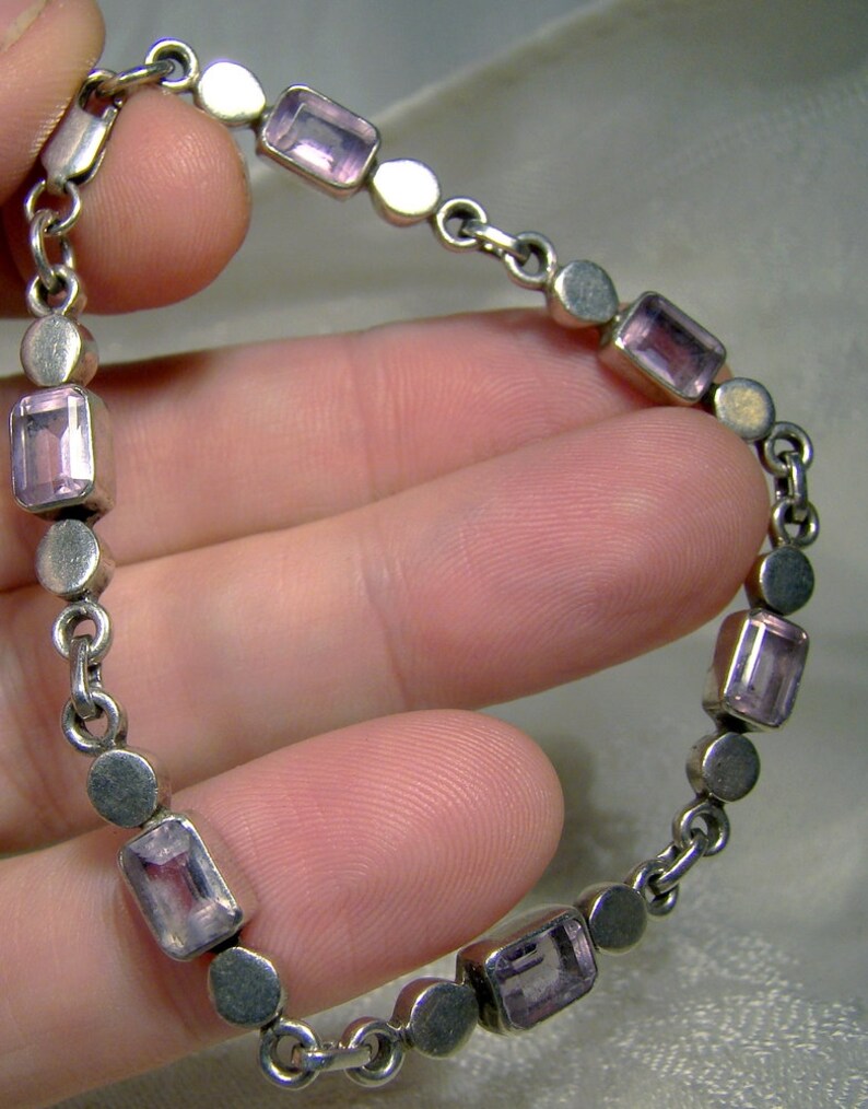 Puede incluir: Un brazalete de cadena de plata con piedras de amatista rectangulares. El brazalete tiene un dise&ntilde;o simple con c&iacute;rculos de plata y piedras de amatista alternos.