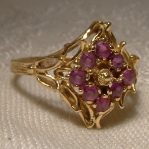 May include: A gold ring featuring a delicate filigree design and a cluster of pink gemstones in the centre.