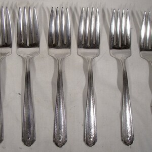May include: Six silver forks with ornate handles. The forks are arranged in a row, with the tines facing up.