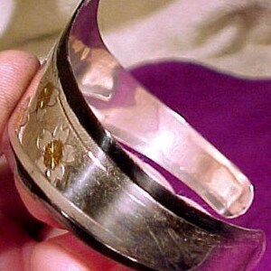 Pu&ograve; includere: Un braccialetto rigido in argento con un design floreale. Il braccialetto &egrave; composto da due pezzi di metallo che sono uniti insieme. Il design &egrave; sul lato esterno del braccialetto ed &egrave; fatto di piccoli fiori in rilievo.