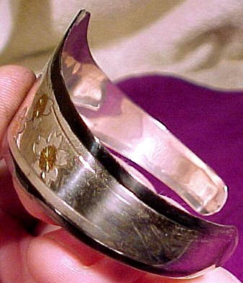 Pu&ograve; includere: Un braccialetto rigido in argento con un design floreale. Il braccialetto &egrave; composto da due pezzi di metallo che sono uniti insieme. Il design &egrave; sul lato esterno del braccialetto ed &egrave; fatto di piccoli fiori in rilievo.