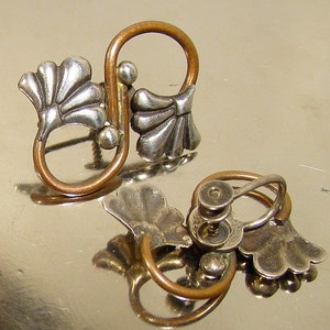 May include: A pair of silver and copper earrings with a floral design. The earrings have a screw-back fastening.