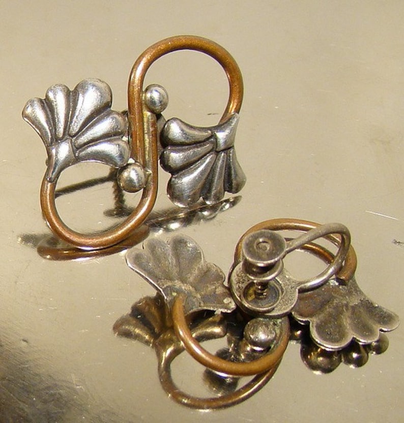 May include: A pair of silver and copper earrings with a floral design. The earrings have a screw-back fastening.
