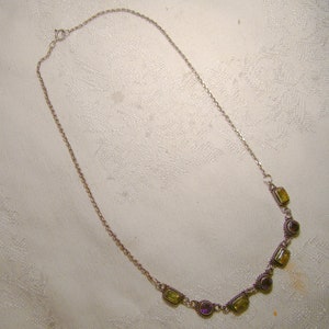 May include: A silver chain necklace with a row of five rectangular green and purple gemstones.