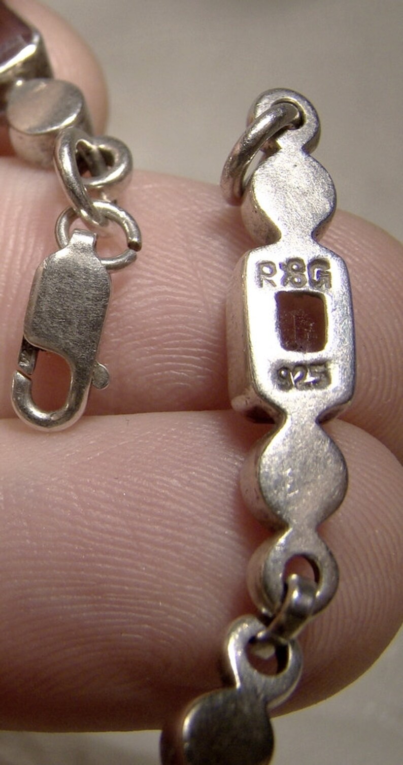 Puede incluir: Un brazalete de cadena de plata con un dije rectangular que dice "R8G 925".