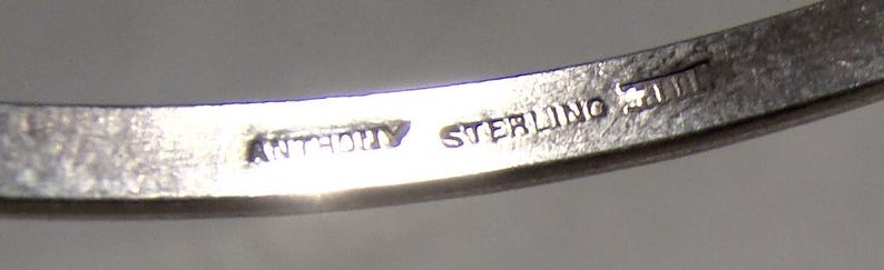 K&ouml;nnte beinhalten: Nahaufnahme eines silbernen Armbands mit dem eingravierten Text "ANTHONY STERLING" auf der Innenseite. Das Armband scheint aus einem gl&auml;nzenden, metallischen Material zu bestehen.