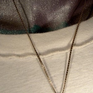 May include: A gold chain necklace with a round pendant featuring a bronze coin with a profile of a woman on it.