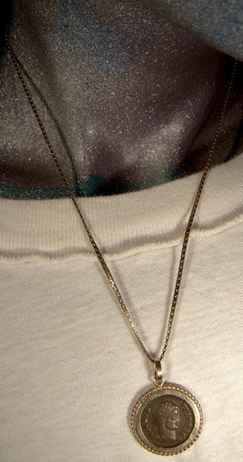 May include: A gold chain necklace with a round pendant featuring a bronze coin with a profile of a woman on it.